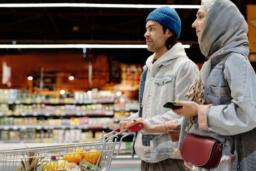 Casal empurrando um carrinho em um supermercado enquanto escolhe frutas e outros alimentos.