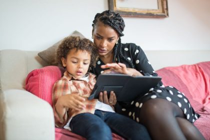 Mãe e filho usam juntos um tablet sentados em um sofá, em casa.