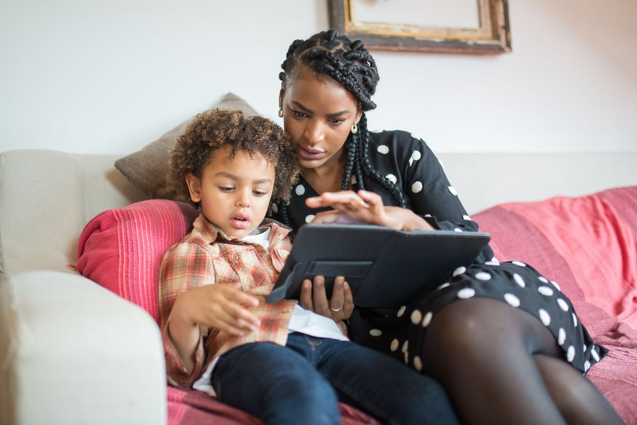 Mãe e filho usam juntos um tablet sentados em um sofá, em casa.