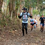 Corredores participam de uma prova de corrida em uma trilha cercada por vegetação.