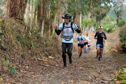 Corredores participam de uma prova de corrida em uma trilha cercada por vegetação.