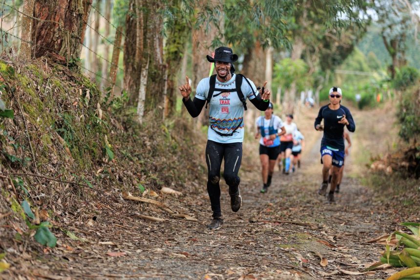 Corredores participam de uma prova de corrida em uma trilha cercada por vegetação.